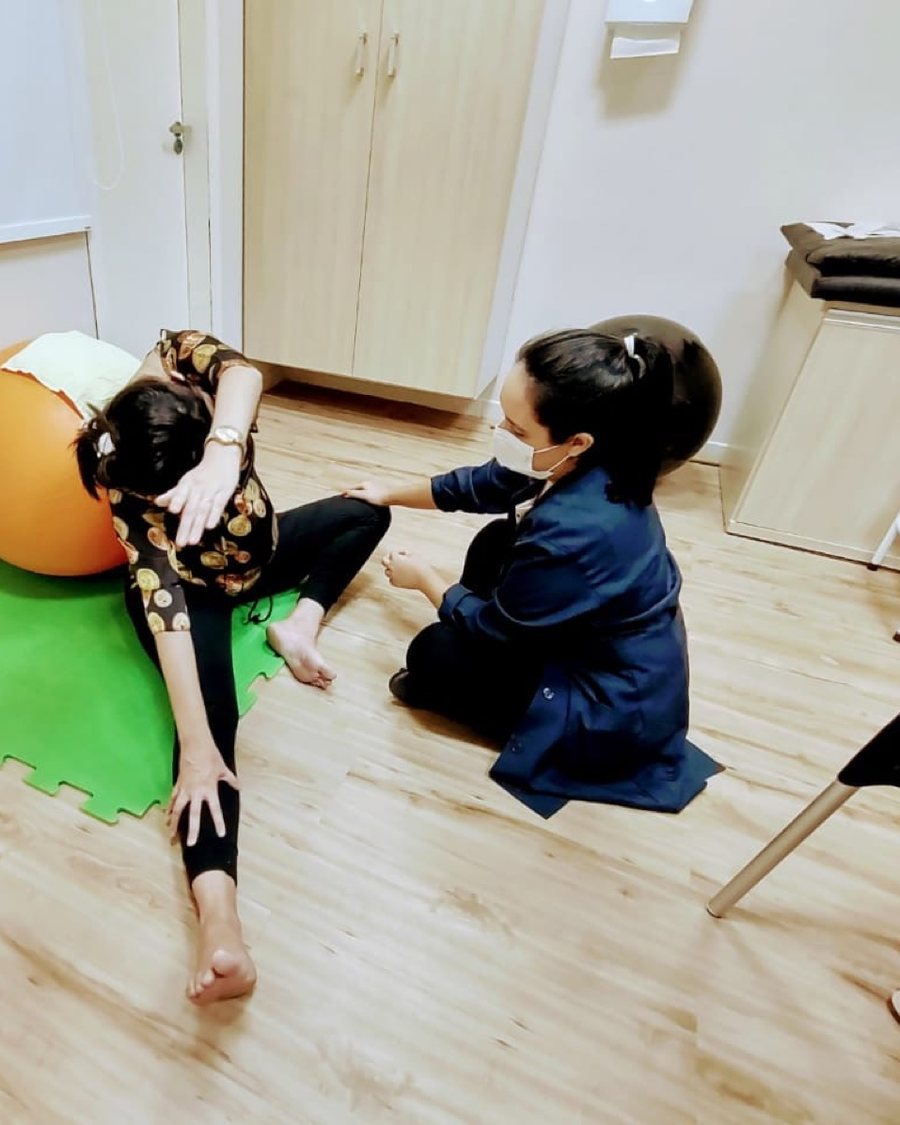 Sessão de fisioterapia do IAAM: a fisioterapeuta orienta um exercício no chão, com a bola, a uma paciente